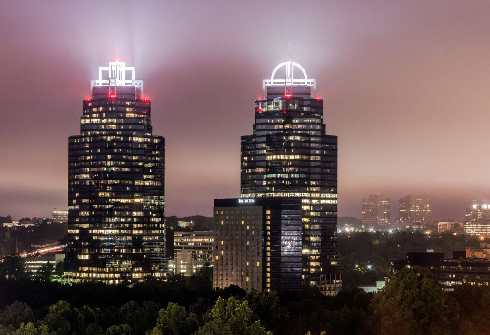 A view of two skyscrapers at night with lights on.